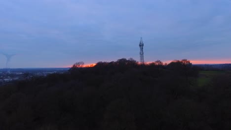 telephone mask on top of a hill surrounded by trees and woodland at sunset dusk moving in drone aerial shot