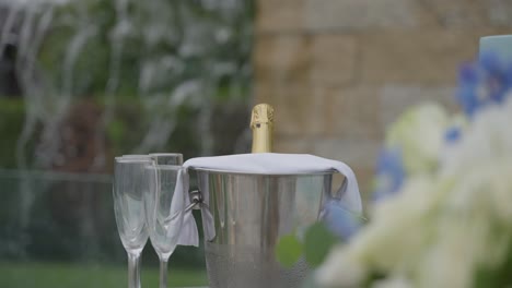 botella de champán refrigerada en un cubo con dos flautas, puesta al aire libre para una celebración, que simboliza el lujo y la festividad