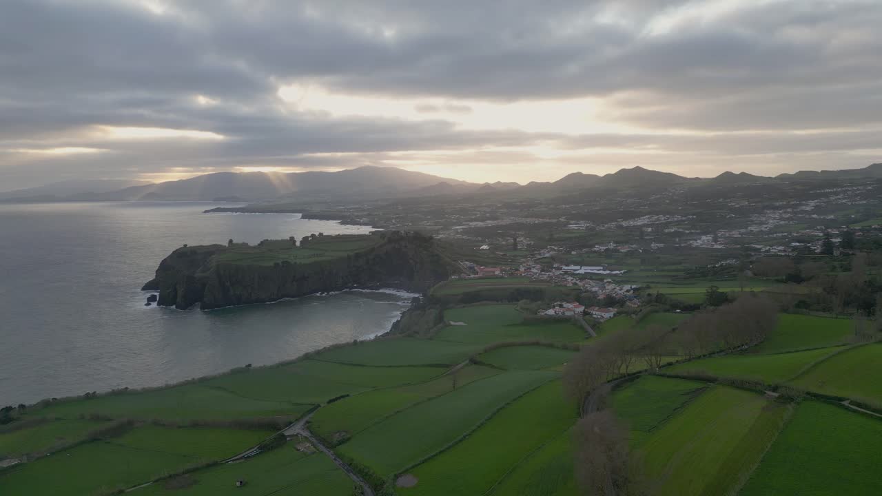 Aerial view of a coastline with green fields and mountains at sunrise