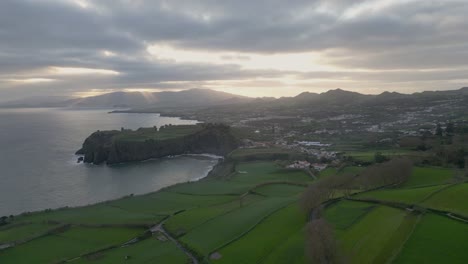 aerial view of a coastline with green fields and mountains at sunrise