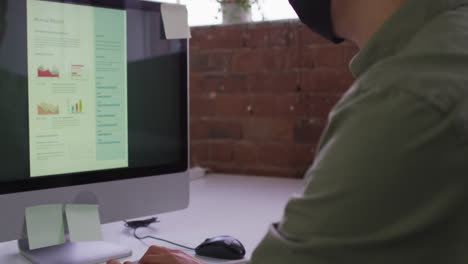Asian-businessman-wearing-mask-sitting-at-desk-using-computer