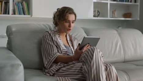 Surprised girl checking bank account on digital tablet computer in living room