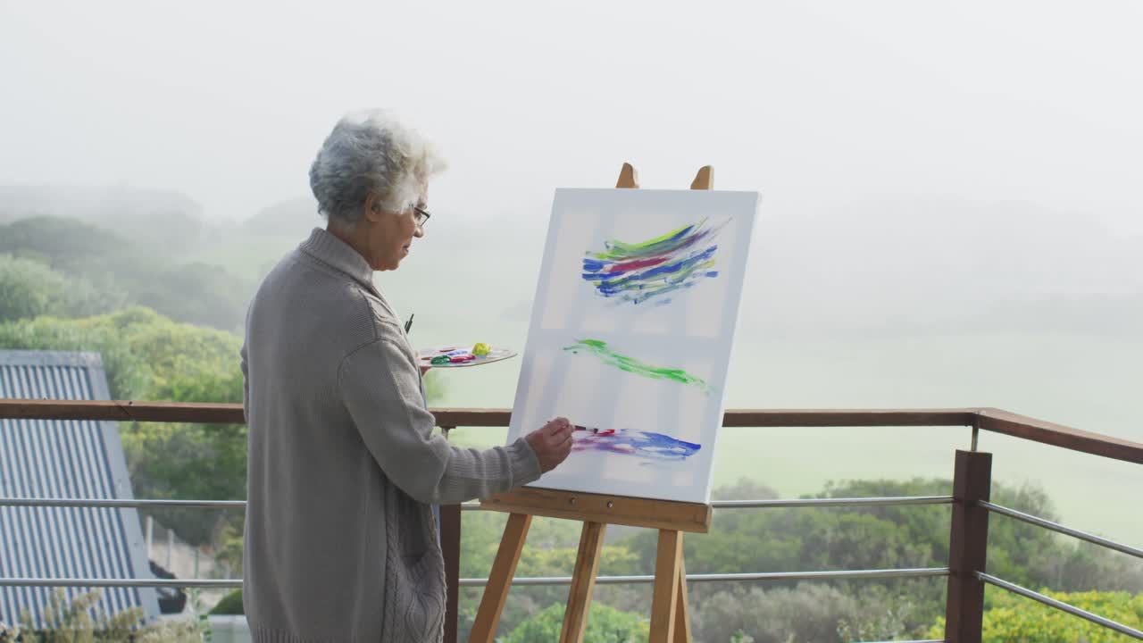 아프리카계 미국인 고령 여성 이 집 의 발코니 에서 캔버스 에 그림 을 그리고 있다
