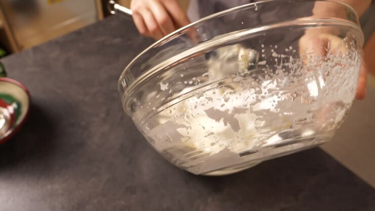 Primo piano ravvicinato di una giovane donna che mescola la schiuma di albume nel composto di burro e miele, preparando una farcitura per torta al miele.