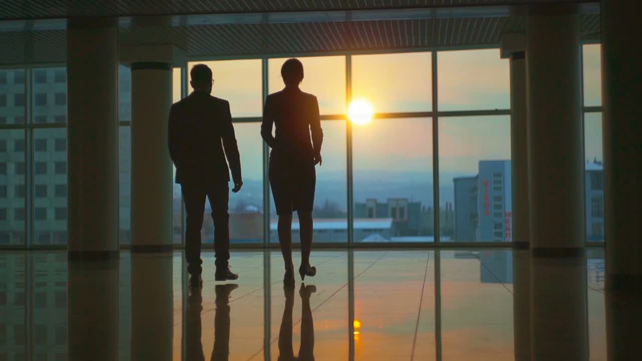 L'uomo e la donna camminano nel corridoio dell'ufficio su uno sfondo al tramonto. Slow motion.