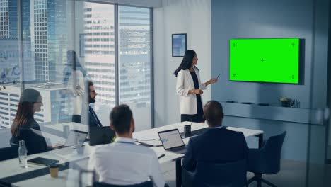 diverse office conference room meeting: successful asian businesswoman uses green screen chroma key wall tv presenting product to group of investors. e-commerce strategy. elevating wide shot