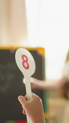 toddler boy shows answer on plastic tag and girl writes on blackboard at home closeup. little brother and sister learn mathematics lesson in class