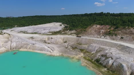 fantastic scenery of an open pit mining. loaded truck with clay going along the road through hilly area. green forest backdrop.