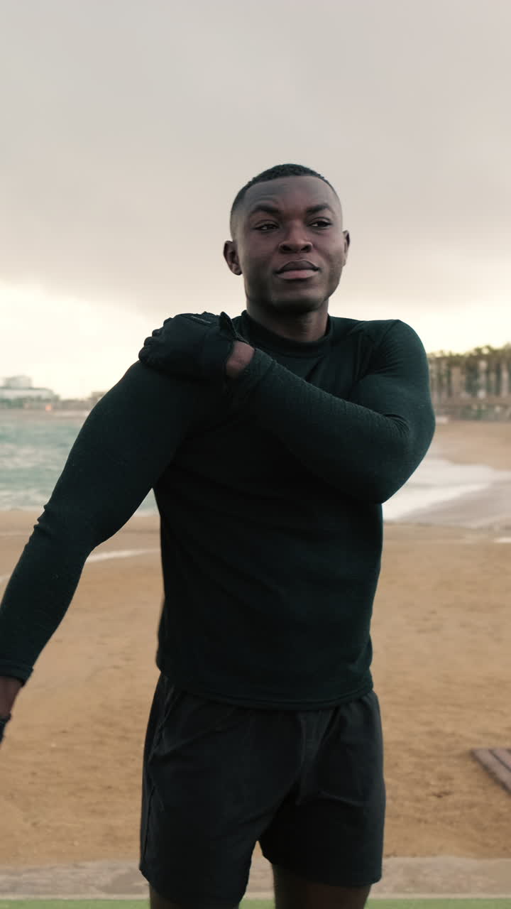 Jonge zwarte man rekt zijn armen op het strand na een training