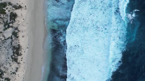 Aerial-top-down-shot-of-foamy-rolling-waves-of-Indian-ocean-reaching-sandy-beach-in-Australia---static-slow-motion-from-above