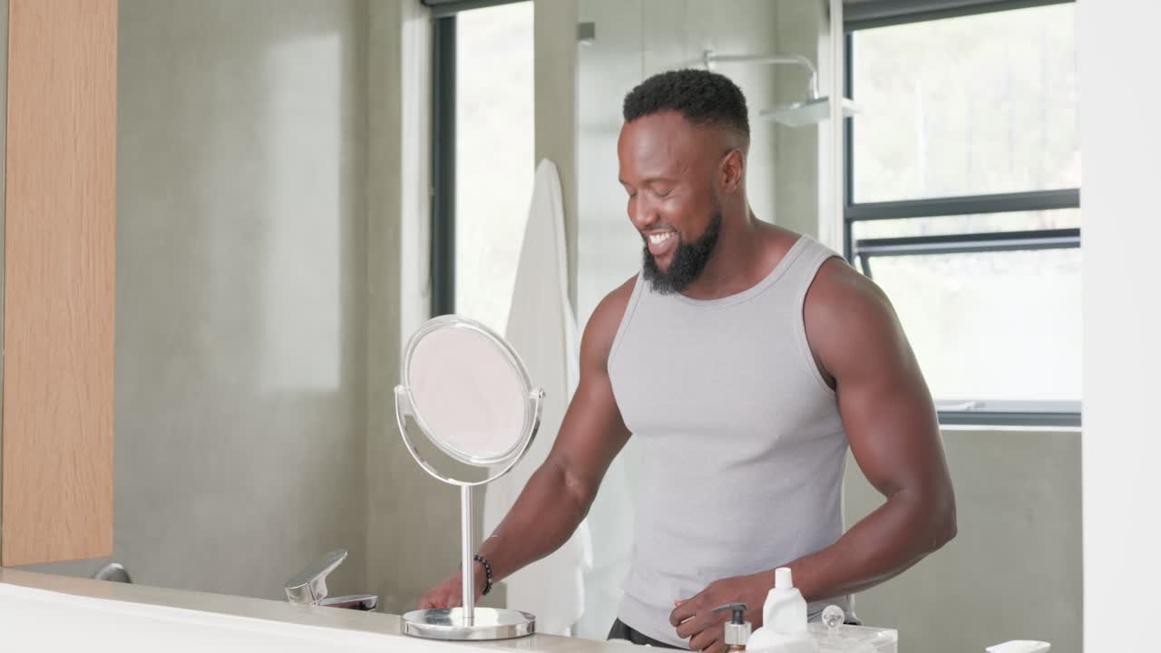 Uomo afroamericano che prende dentifricio e spazzolino al lavandino, si lava i denti e si guarda allo specchio per la cura personale.