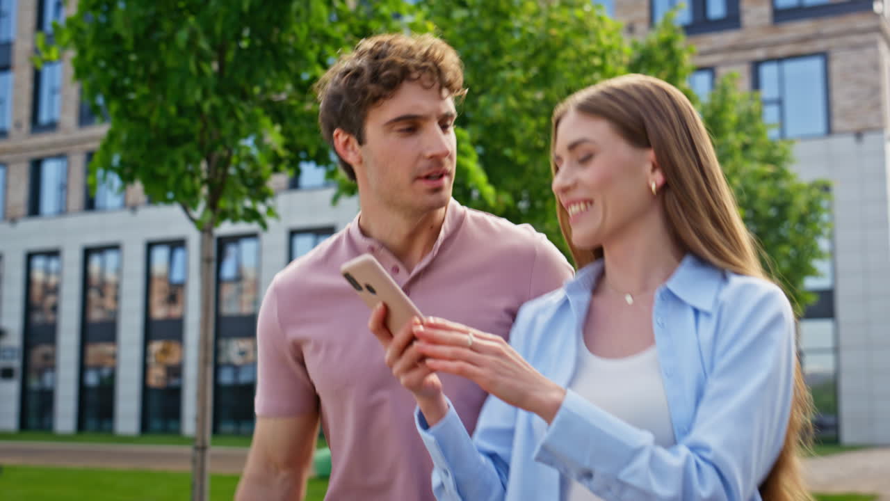 Smiling couple looking smartphone walking street together closeup