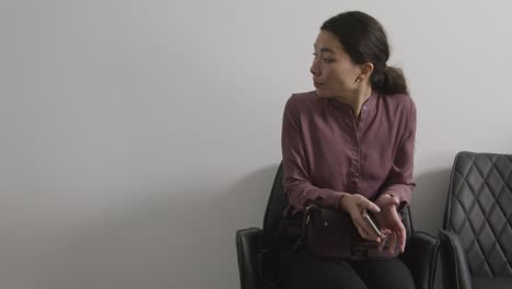 female candidate wearing suit in office waiting for job interview looking at mobile phone