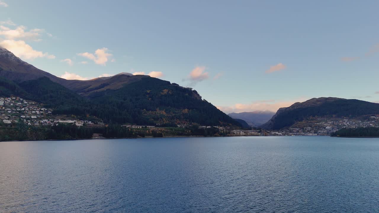 A tranquil lake surrounded by mountains under a clear sky, captured in Queenstown, New Zealand