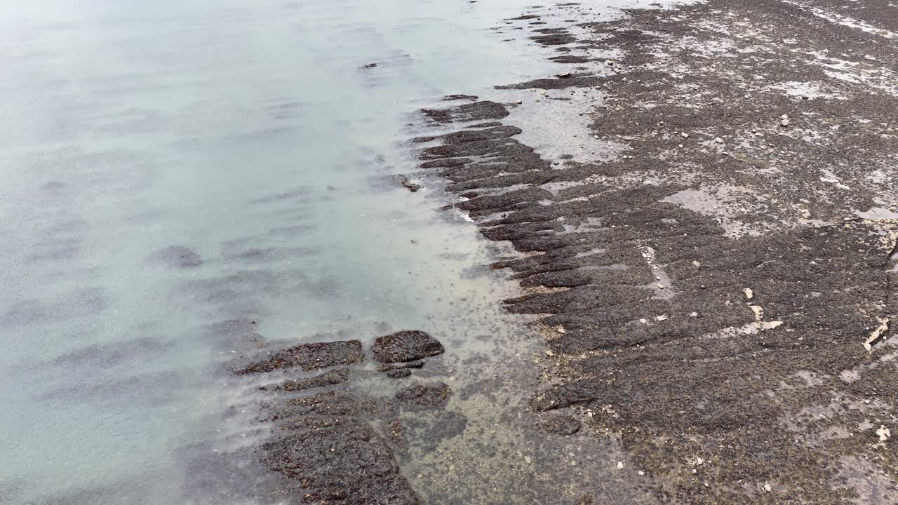 Panoramica diurna nuvolosa su una costa rocciosa e strutturata, pozze di marea e acque basse durante la bassa marea