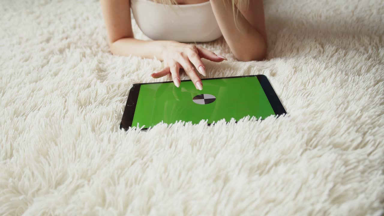 la mujer está acostada en la alfombra con una tableta con pantalla chromakey y desliza su dedo en la pantalla táctil, primer plano, vista frontal. concepto aplicación móvil