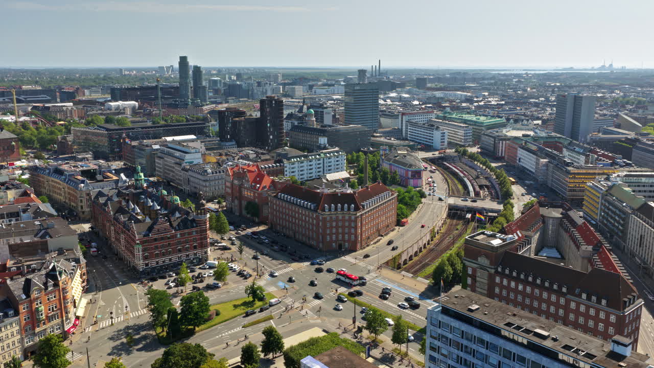 Dronebillede af et travlt vejkryds med biler, busser, cyklister og et rødt S-tog, der passerer gennem centrum