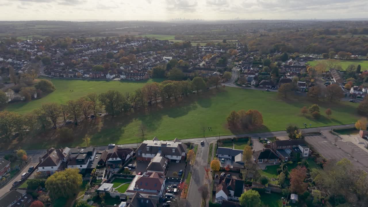 Drone orbits Theydon Bois facing toward London’s skyline. As altitude drops slightly, more of the distant city becomes visible. Foreground shows the village green, trees and surrounding houses