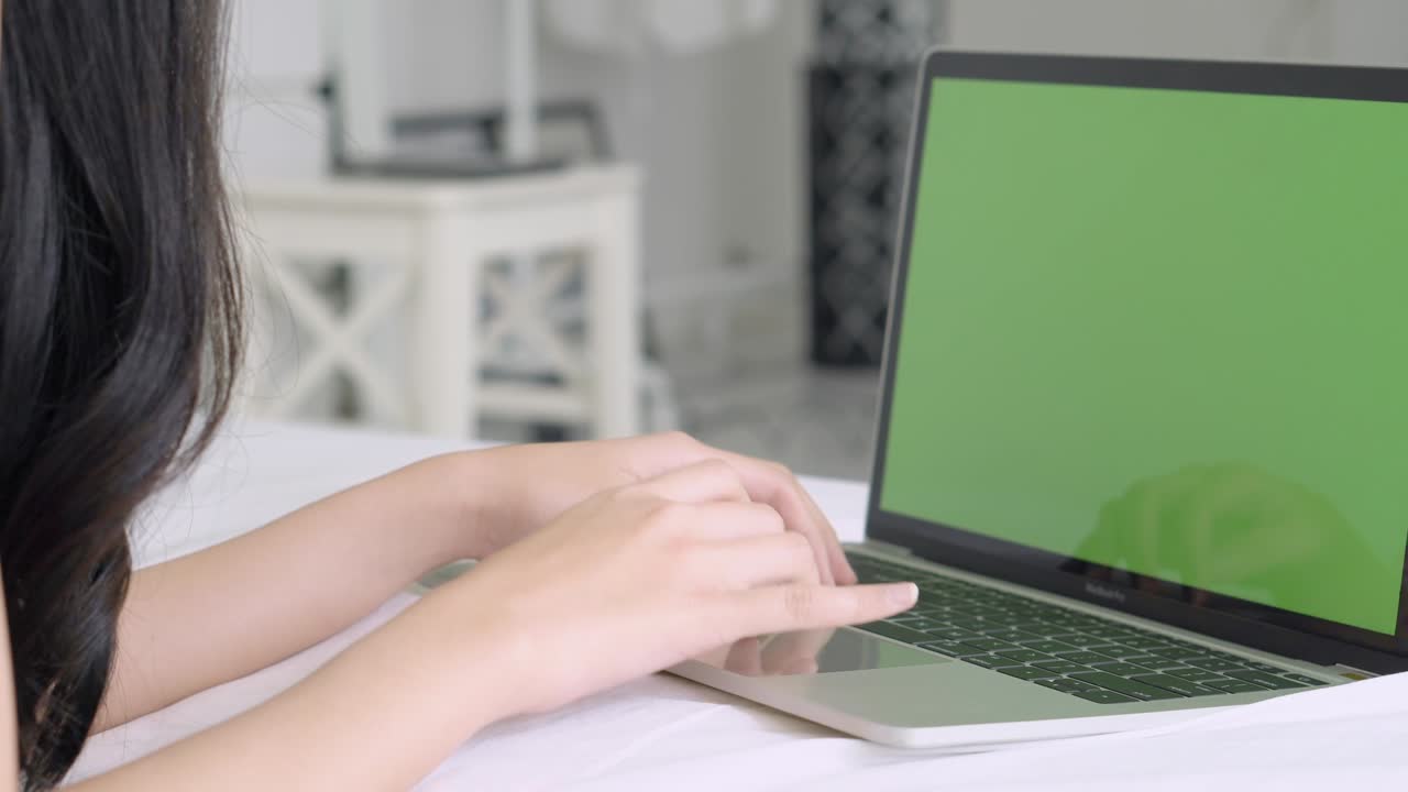 vista de fondo de primer plano joven asiática escribiendo en una computadora portátil con pantalla verde en la cama en casa, chica acostada usando trabajo con portátil con llave de croma, comunicación y concepto de negocio.