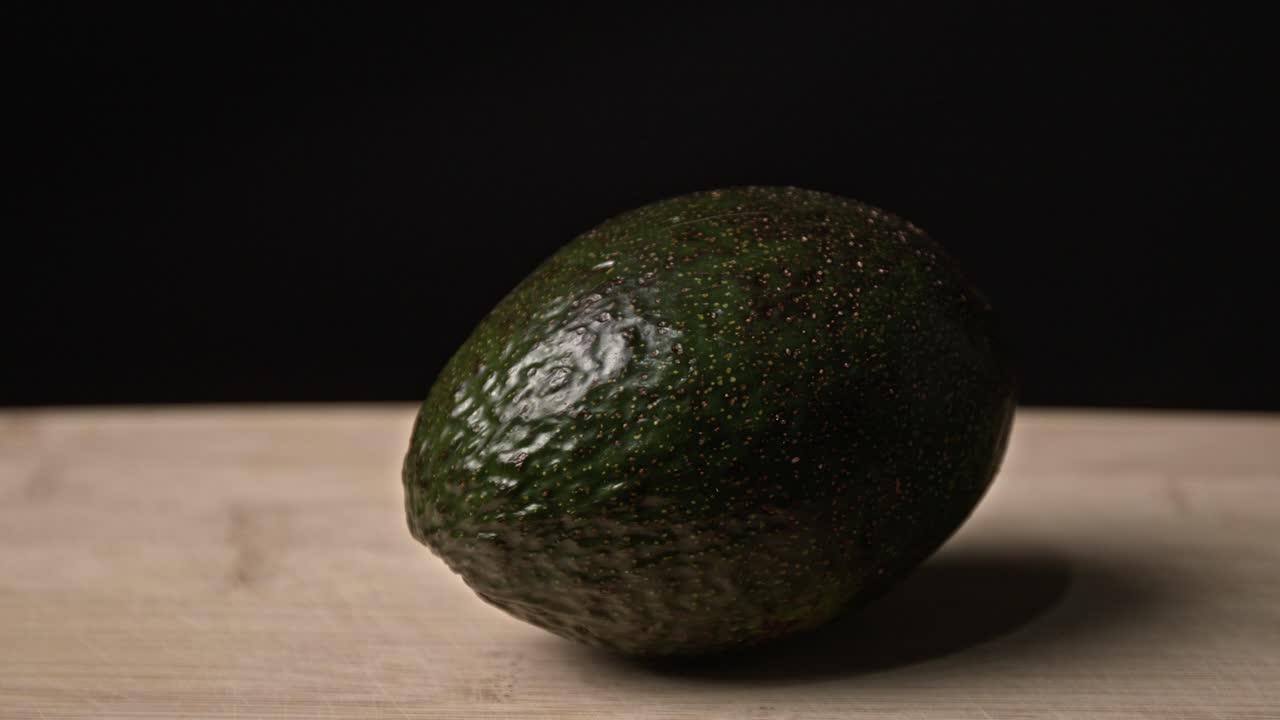 Close-up of a fresh avocado placed on a wooden table in a dark ...