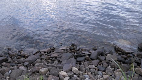 pebbles and rocks along a lake shore with wave washing on a quiet summer day