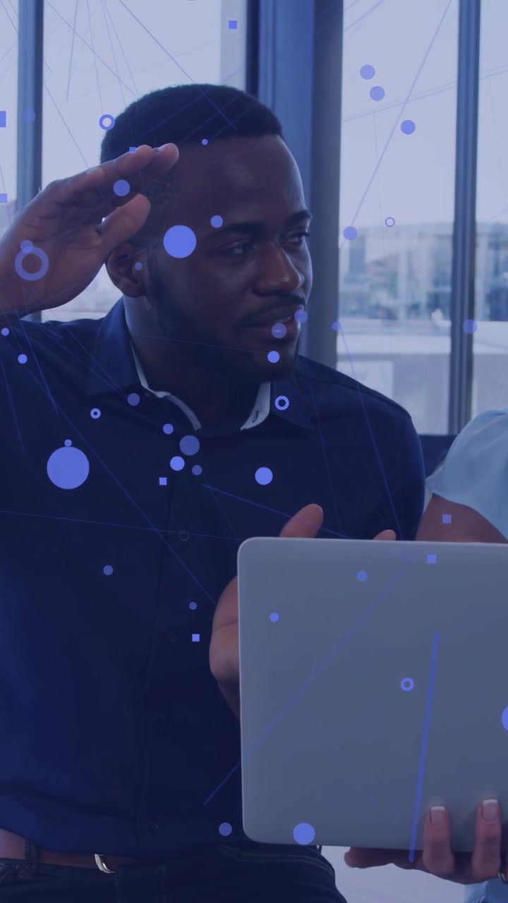 Vertical video: Manager gesturing to business data while peer holding laptop, blue overlaying faces