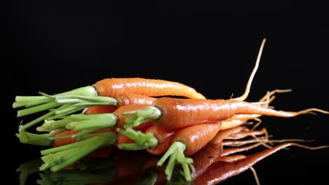 a bunch of baby carrots rotates smoothly on a glossy black surface, highlighting their vibrant color and fresh texture