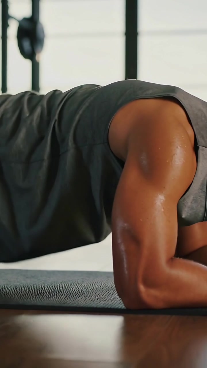 Vertical video: Lowering to forearm plank, man holding core at gym, with grip mat and dark gray top