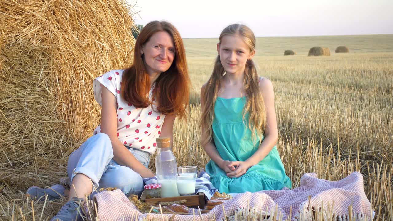 happy family in a wheat field. mother and daughter on a picnic in a wheat field near one of round bales at sunset time