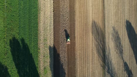 aerial view of farmer tractor with seedbed cultivator on agricultural farmland parcels for cultivation, spring seeding