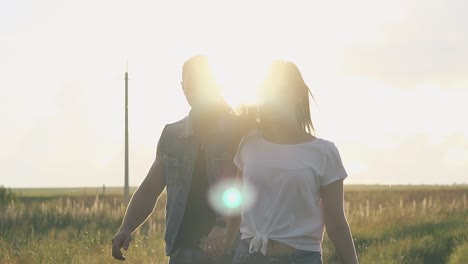 vista cercana pareja iluminada por el sol camina en el campo bajo el cielo naranja