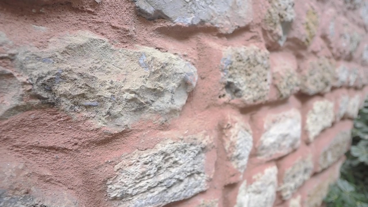 Vista detalhada de um muro de pedra antigo com pedras texturizadas e argamassa rosa