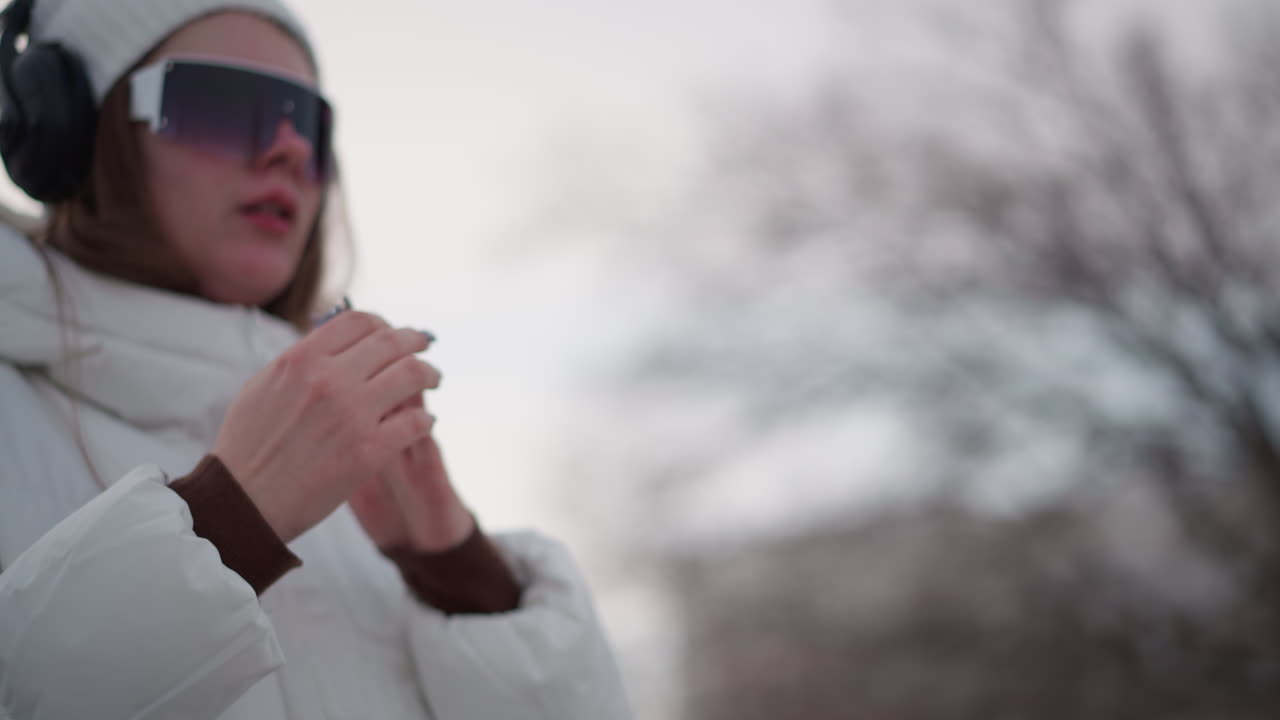 Youth demonstrates hand dance moves while smiling in winter coat and headphones against outdoor tiled pavement backdrop under pale sky capturing playful motion energy
