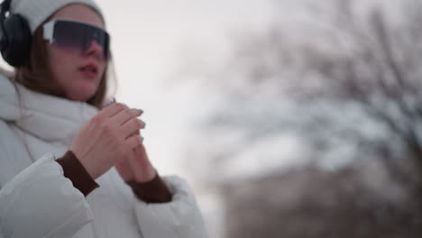 youth demonstrates hand dance moves while smiling in winter coat and headphones against outdoor tiled pavement backdrop under pale sky capturing playful motion energy