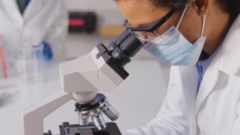 close up of female lab worker or phlebotomist analysing blood samples in laboratory with microscope