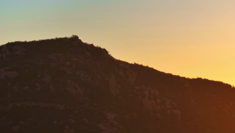 aerial-view-of-the-top-of-a-cowles-mountain-in-san-diego-ca-during-a-beautiful-yellow-red-sunset,-orbit-wide-shot