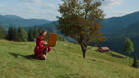 Inspired-girl-creating-picture-on-green-hill.-Woman-painting-sketch-on-easel.