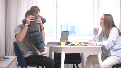 parents sitting at a table and their baby is near them on the floor