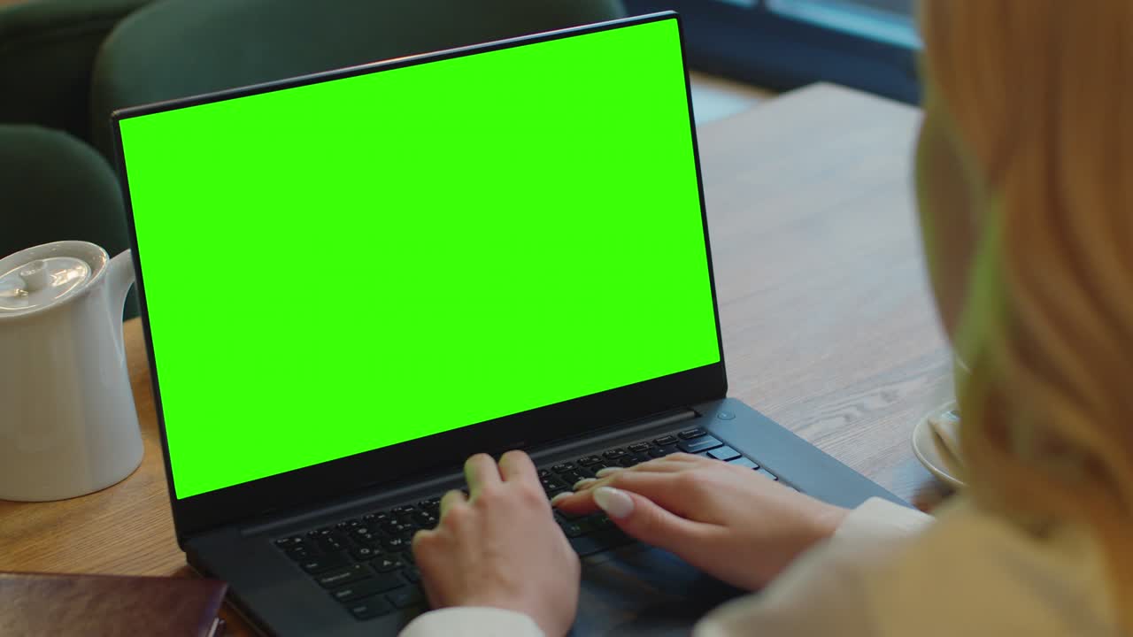Woman hands using laptop with blank green screen sitting in cafe. Chroma key mock-up display for free content.