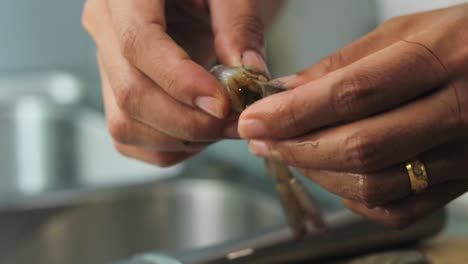 a skinless raw shrimp being broken in half and then a woman is making a deep cut in its body to remove its stomach