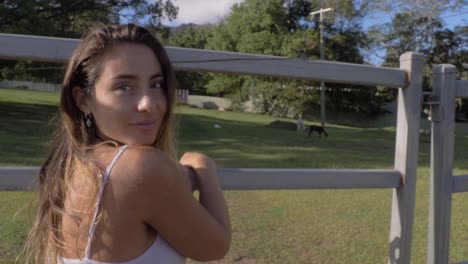 smiling young caucasian woman leaning on fence admiring llamas on field - fauna at currumbin valley, gold coast, qld, australia