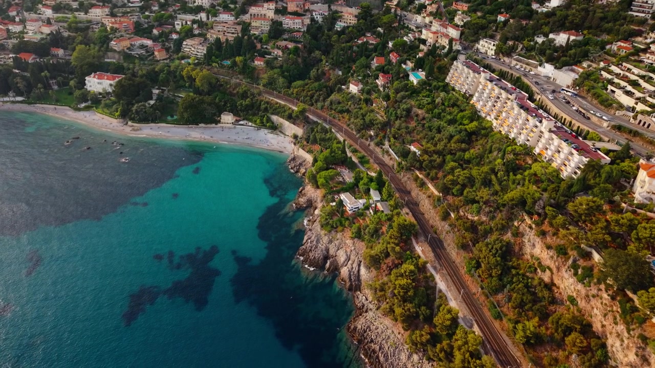 Drone rivolto verso il basso vola sopra una ferrovia costiera verso una spiaggia turchese.