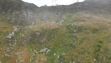 Fliegen-über-Die-Bergwiesen-Der-Felsigen-Alpen-Mit-Spuren-An-Einem-Nebligen-Tag-In-Passo-San-Marco,-Norditalien---Luftdrohne,-Rückzugsaufnahme