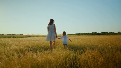 mother and child walking hand-in-hand through a golden field at sunset