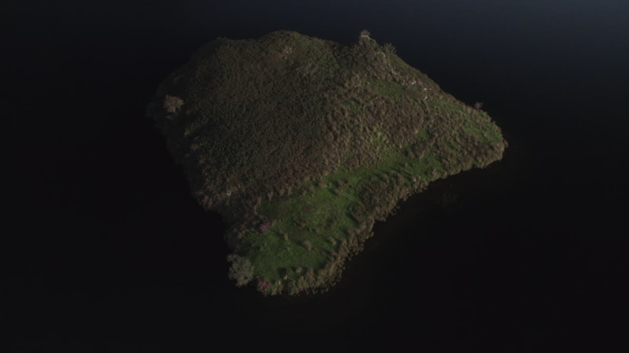 Drone aerial zoom out of small island in Llyn y Dywarchen lake, North Wales. Also known as Turf Island or Floating Island, this scenic landscape is a unique travel and nature destination