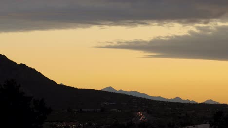 Bunte-Bergige-Wüstenlandschaft-Bei-Sonnenuntergang-Mit-Autos,-Die-Langsam-Auf-Der-Straße-Fahren