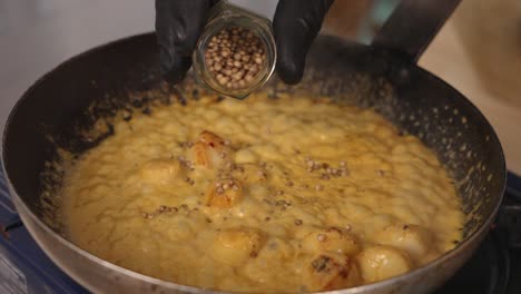 chef profesional añadiendo semillas de cilantro en coco curry vieiras plato de mariscos, cocinar en la sartén, hirviendo para resaltar el sabor de las especias, haciéndolas florecer con olor aromático