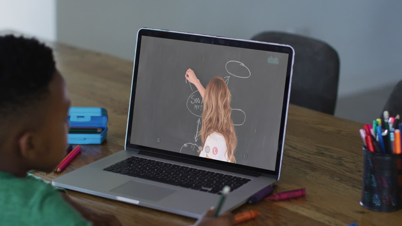 niño afroamericano haciendo una videollamada en una computadora portátil mientras hace la tarea en casa
