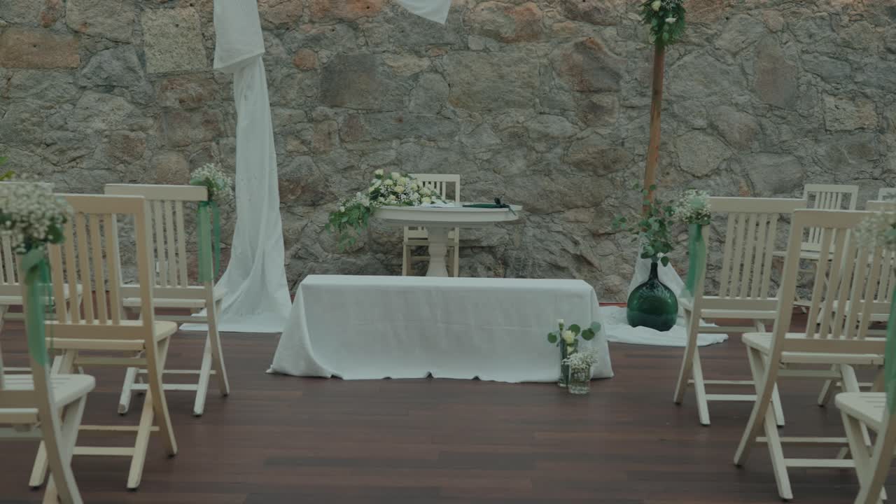Outdoor wedding ceremony setup with white chairs and stone wall backdrop
