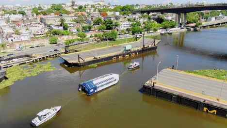 Interceptor-004-in-aerial-shot-in-operation-on-the-ozama-river,-dominican-republic,-clear-day-floating-bridge,-brown-waters